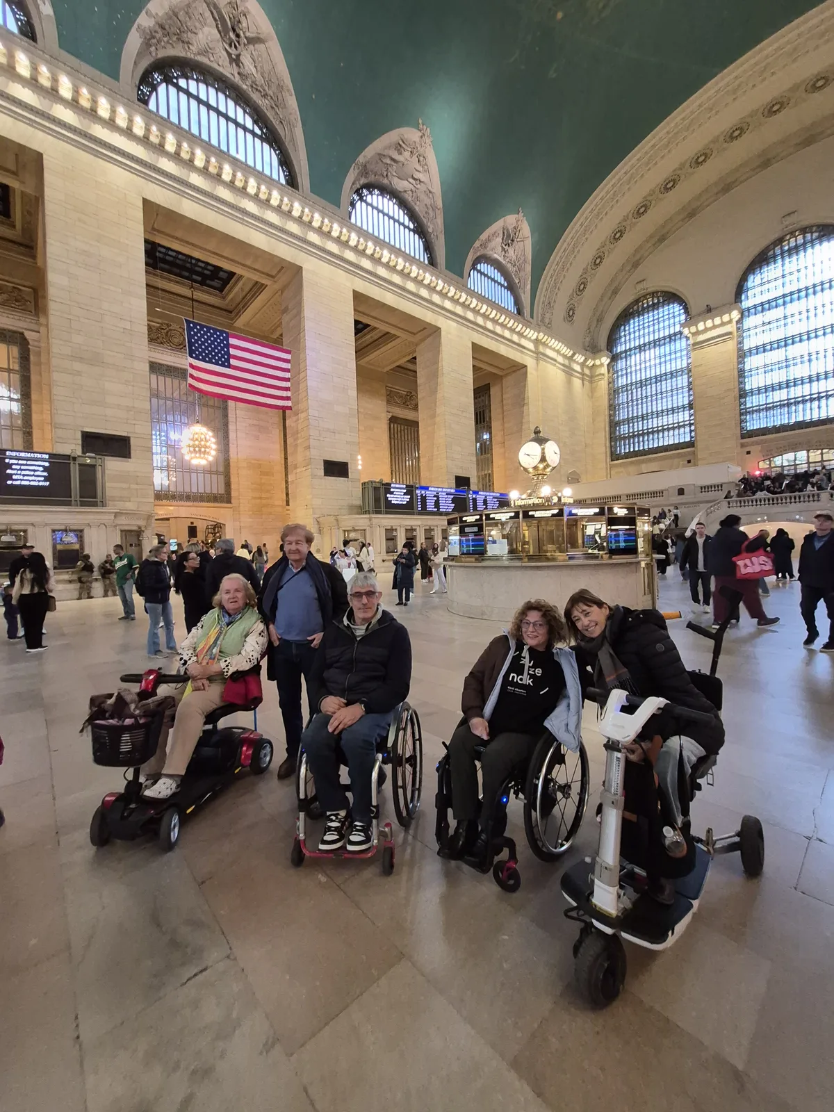 Gran terminal de transporte con bóvedas arquitectónicas, personas en sillas de ruedas circulando por el piso plano, ambiente amplio y bien iluminado.
